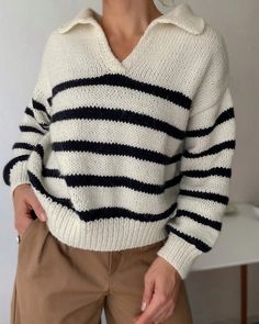 a woman wearing a white and black striped sweater is standing in front of a wall