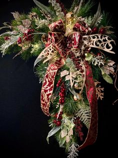 a christmas wreath with red and gold ribbons, holly berries, pine cones, evergreen leaves and other greenery