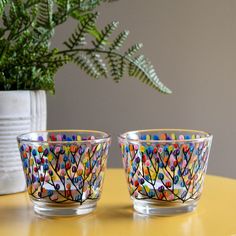 two glass bowls sitting on top of a yellow table next to a potted plant