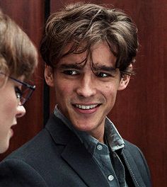 a young man in glasses and a suit smiling next to another person with short hair