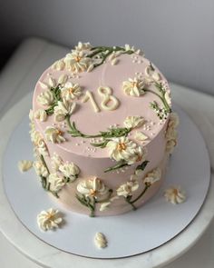 a pink cake with white flowers and the number eighteen on it's top is sitting on a plate