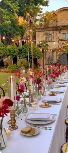 a long table is set with flowers and candles for an outdoor dinner party in the garden