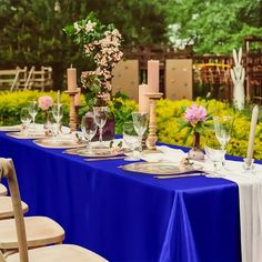 a long table with blue cloth and white linens is set for an outdoor dinner