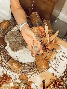 a woman is making a wreath out of twigs and leaves on a table with other autumn decorations