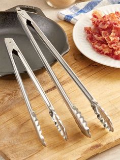 four stainless steel utensils sitting on top of a cutting board next to a plate