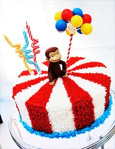 a red, white and blue birthday cake with a monkey on top that is decorated with balloons