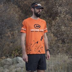 a man in an orange shirt and black shorts is standing on the ground with his skateboard