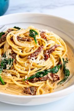 a white bowl filled with pasta and spinach on top of a marble countertop