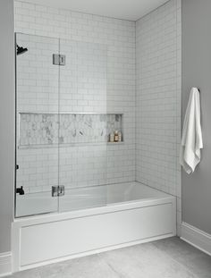 a white tiled bathroom with a walk in shower next to a bathtub and towel rack