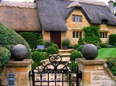 an iron gate in front of a stone house with thatched roof and garden area