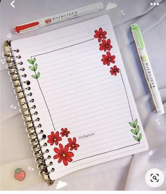 an open notebook with red flowers on it next to a green pen and eraser