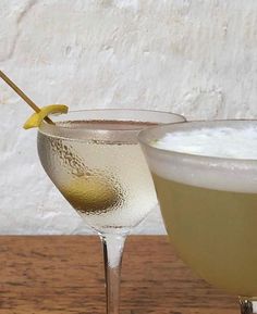 two glasses filled with drinks sitting on top of a wooden table