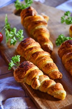 several croissants on a cutting board with parsley and tomatoes in the background