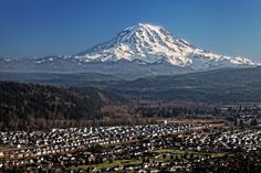 a large snow covered mountain towering over a small town in the foreground with houses and trees below