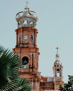 an old building with a clock on the top and a cross at the top is surrounded by palm trees