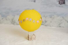 a yellow paper lantern sitting on top of snow covered ground