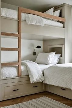 two bunk beds with white sheets and pillows in a small room next to a window