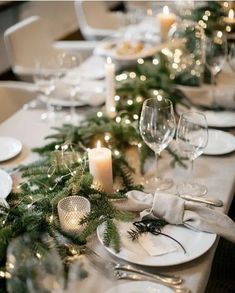 the table is set with white plates, silverware and greenery for an elegant christmas dinner