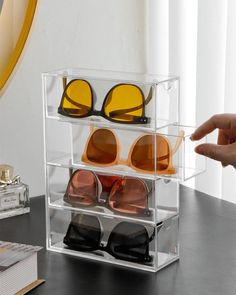 a clear display case holding sunglasses and reading glasses on a desk next to a book