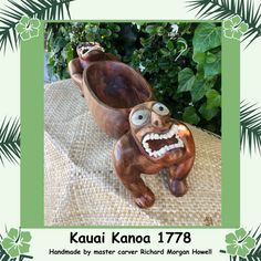 a wooden statue of a monkey with its mouth open and eyes wide open, sitting in front of a bush