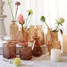 several vases with flowers in them on a table next to candles and a candle holder