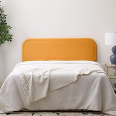 a white bed with an orange headboard next to a potted plant and lamp