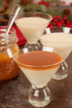 three glasses filled with liquid sitting on top of a table next to jars and spoons