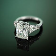 an engagement ring with a princess cut diamond in the center on a reflective surface against a green background