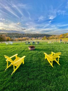 two yellow lawn chairs sitting on top of a lush green field next to a fire pit