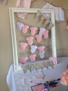 a baby shower party with pink and green items on the table, including clothes hanging from a line