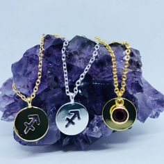 three different necklaces sitting on top of a rock with purple crystals in the background