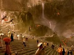 many people are walking up and down the stairs in front of a waterfall while holding umbrellas