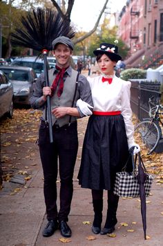 a man and woman dressed in costume standing next to each other on a sidewalk with umbrellas