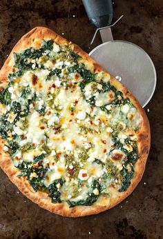 a pizza sitting on top of a pan covered in cheese and spinach next to a spatula