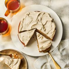 a white plate topped with a cake covered in frosting next to two cups of tea