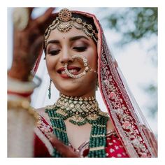 a woman in a red and green bridal outfit smiles while holding her hands up to her face