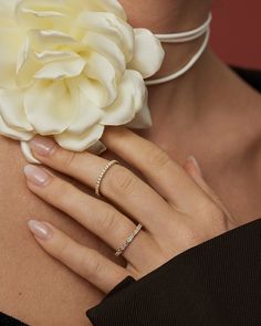 a woman wearing a necklace and ring with a large flower on her neck, holding onto the back of her hand