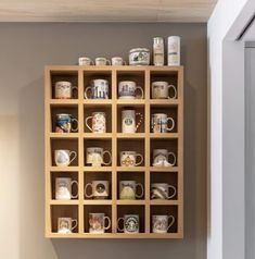 a wooden shelf filled with coffee mugs on top of a wall next to a window