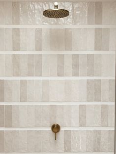 a white tiled shower with a gold faucet and hand held shower head in the corner