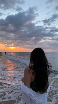 a woman standing on top of a sandy beach next to the ocean at sun set