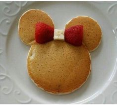 a mickey mouse pancake on a white plate with a red bow in the middle