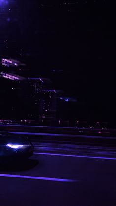 a car driving down the road at night with its headlights on and buildings in the background