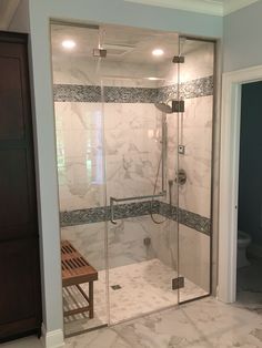 a walk in shower sitting inside of a bathroom next to a wooden bench on the floor