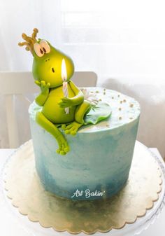 a green frog sitting on top of a cake with a lit candle in it's mouth