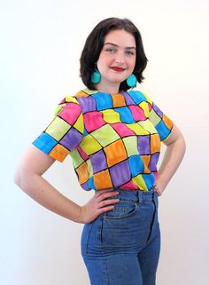 This is a sweet colorful 90s vintage "Notations" top! It's a bright color block geometric square print in shades of pink, blue, yellow, purple and orange with black grid lines. A short sleeved pullover, it has a boxy shape, a high round neckline, no shoulder pads, and it closes with a back keyhole neckline and a black button and loop. The fabric is a lightweight silken polyester.This top is in very good clean vintage condition, no flaws noted. The label says "Notations, Size S, 100% Polyester, M Retro Multicolor Tops With Rainbow Print, Retro Spring Top With Rainbow Print, Retro Rainbow Print Top For Spring, Retro Multicolor Rainbow Print Top, Retro Plaid Top With Graphic Print, Retro Multicolor Tops With Vibrant Print, Retro Multicolor Top With Vibrant Print, Trendy Multicolor Retro Print Top, Trendy Multicolor Top With Retro Print