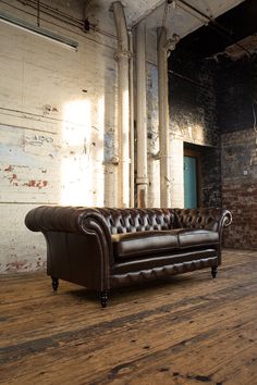 a brown leather couch sitting on top of a wooden floor next to a brick wall