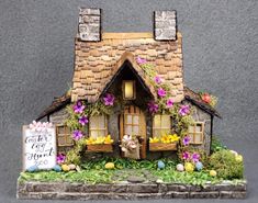 a miniature house is decorated with flowers and greenery for the front door to welcome guests