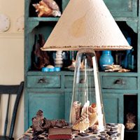 a lamp that is on top of a table with shells in the bottom and an open book underneath it