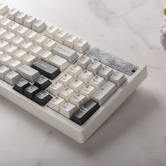 a white and black keyboard sitting on top of a marble table next to an orange vase