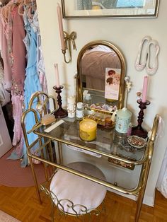 a vanity with a mirror, candles and other items on it in a room filled with clothes